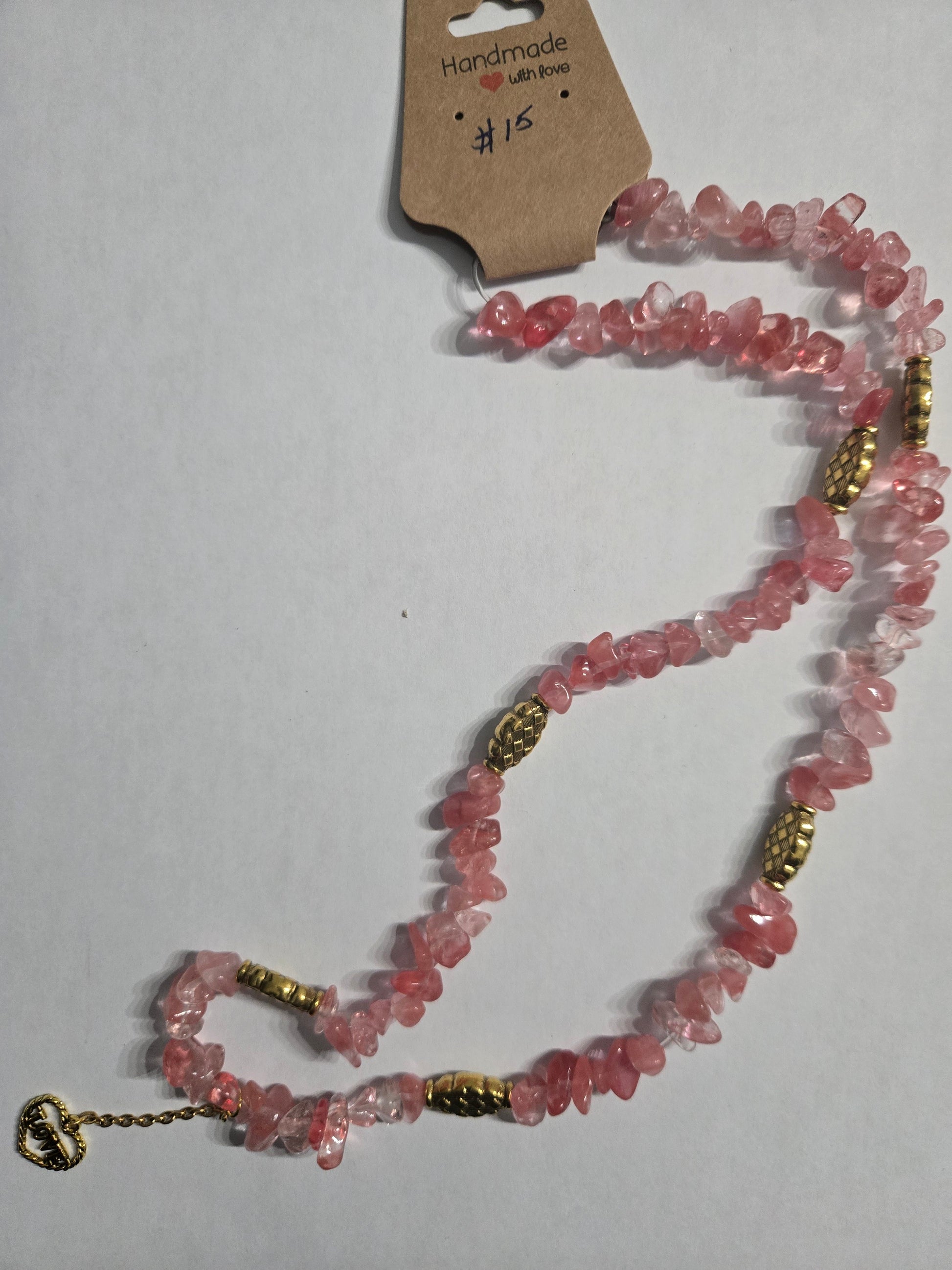 Handmade necklace with pink stone charms, accented with gold in color charms, and having a gold in color heart charm with "LOVE" as a focal point.