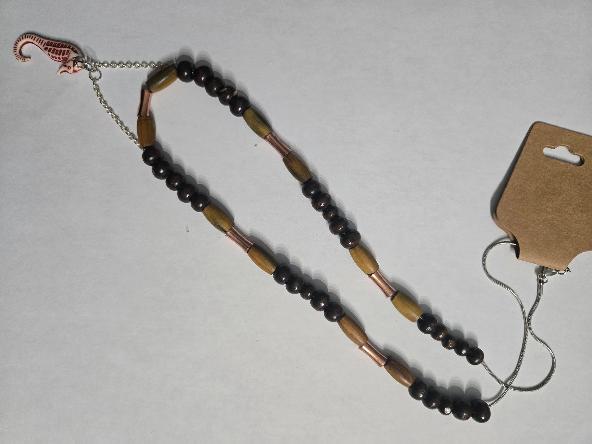 Handmade beaded necklace with brown wooden beads, accented with tan wood and brass spacer beads, and having a seahorse pendant as a focal point.