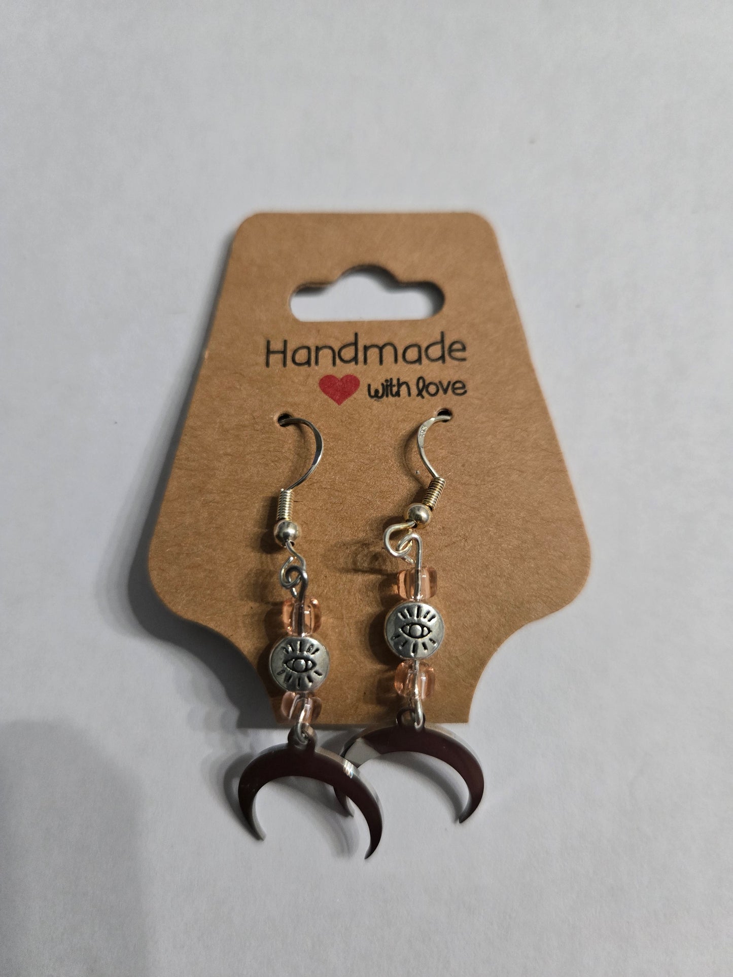Handmade earrings with silver in color metallic crescent moon charms, accented with amber glass beads and silver in color "All Seeing Eye" beads, and crafted on sterling silver earring facets.