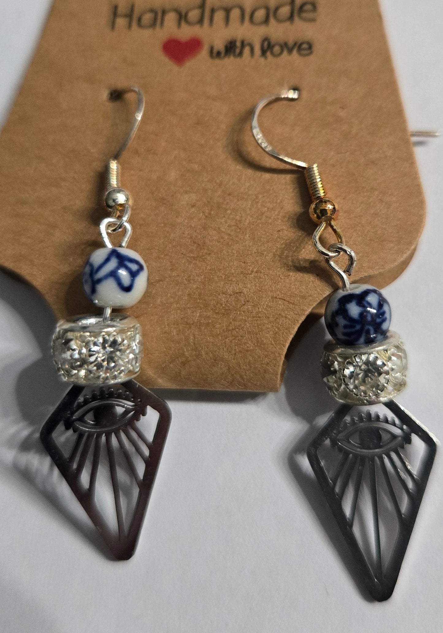Handmade earrings with pewter "All Seeing Eye" charms, accented with blue / white glass beads, as well as silver in color beads encrusted with simulated CZ stones, and crafted on sterling silver earring facets.