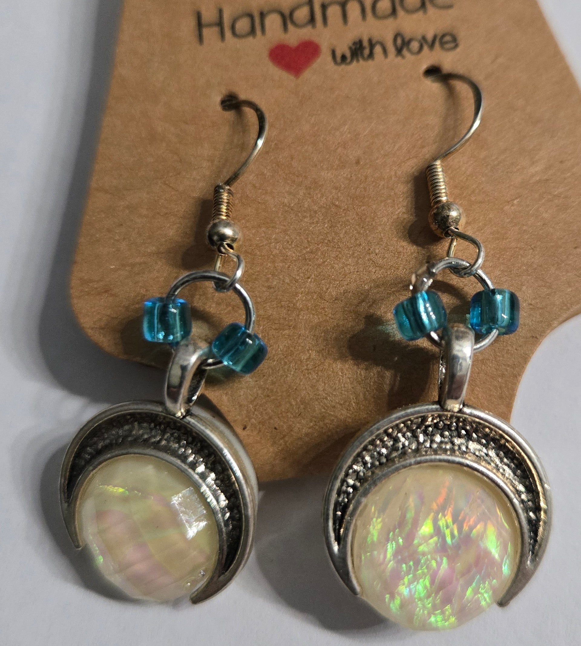 Handmade earrings with pewter crescent moon charms, accented with blue glass beads, and crafted on sterling silver earring facets.