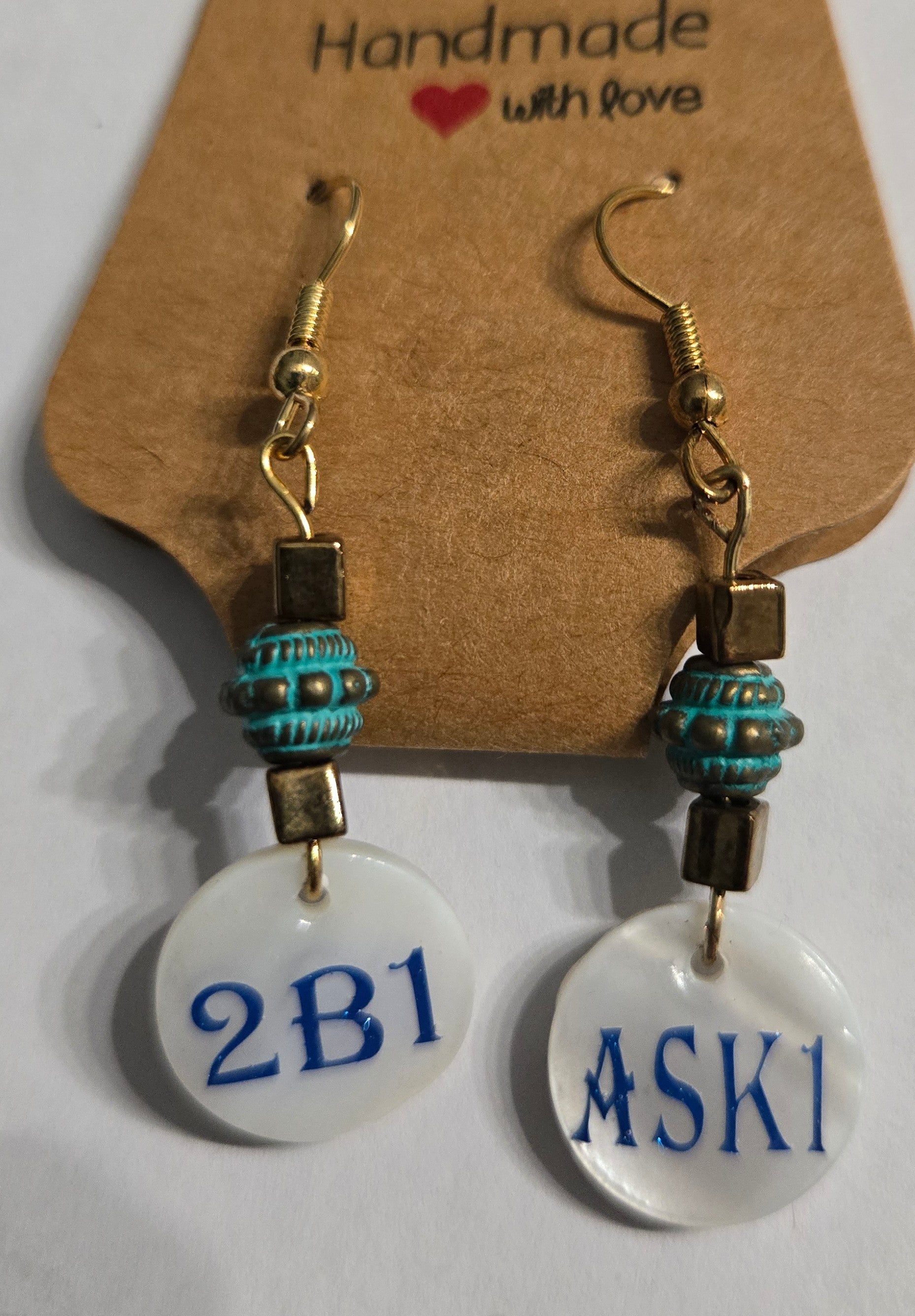 Handmade earrings with faux pearl charms bearing the text of "2B1" and "ASK1", accented with gold and blue metallic beads.