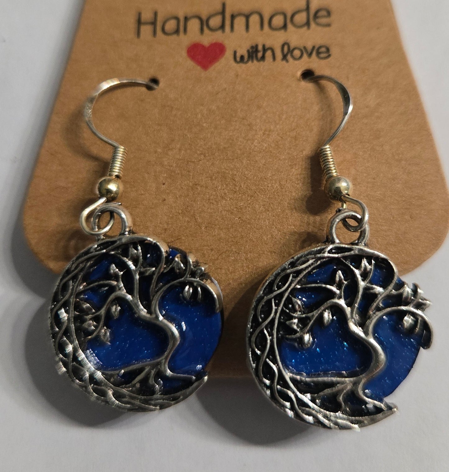 Handmade earrings with pewter "Tree of Life" charms with a blue resin accent, and crafted on sterling silver earring facets. 