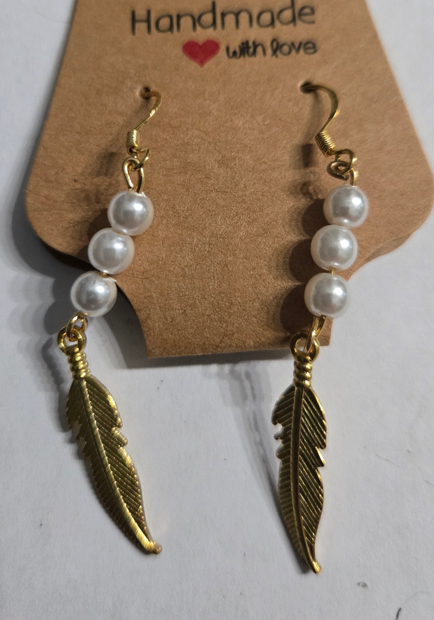 Gold plated earrings with round faux pearl beads, accented with gold metallic feather charms.