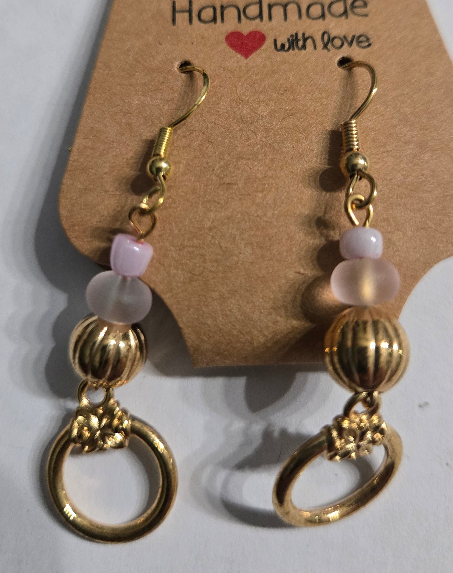 Gold plated earrings with round frosted and white beads, accented with gold metallic hoop charms.