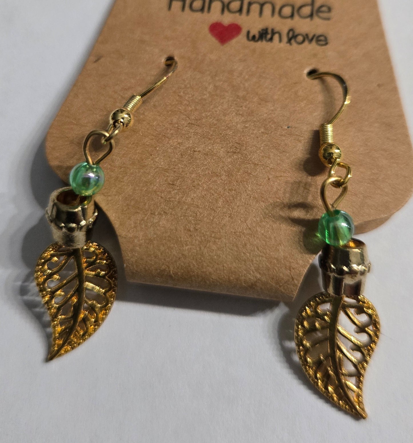 Gold metallic earrings with green glass beads, and gold metallic leaf charms.